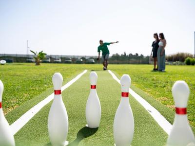 Menschen spielen draußen auf einem Rasen Bowling mit großen Pins.
