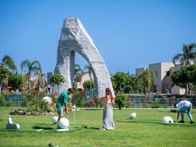 Urlauber spielen Minigolf vor einer Felsstruktur auf einer sonnigen Hotelanlage.