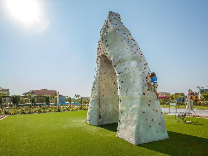 Große Kletterwand auf grünem Rasen unter sonnigem Himmel in einem Freizeithotel.