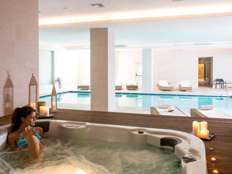 Frau entspannt in einem Whirlpool mit Blick auf einen Innenpool im Hotel.