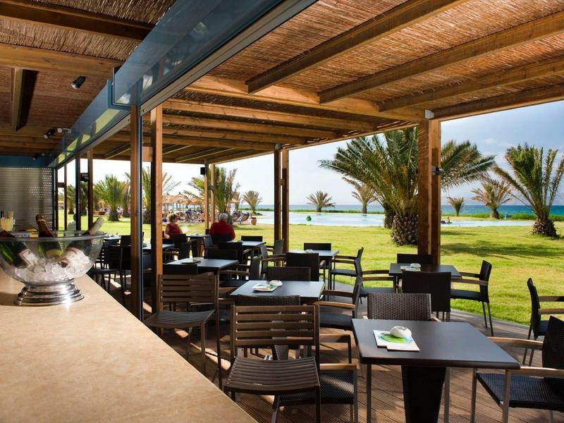 Überdachte Außenterrasse mit Tischen und Stühlen mit Blick auf den Garten und das Meer.