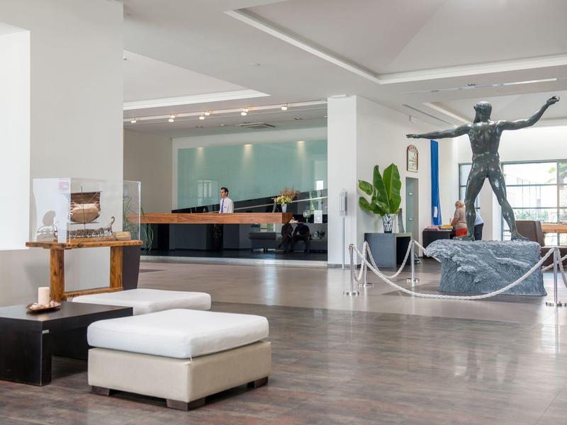 Moderne Hotellobby mit weißen Sitzmöbeln, Empfangstresen und großer Skulptur.