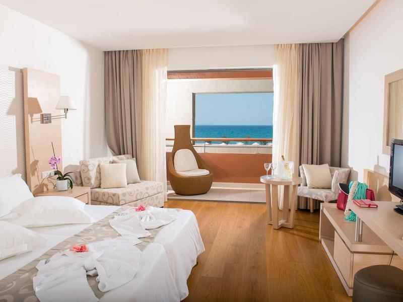 Modern eingerichtetes Hotelzimmer mit Doppelbett, Sitzbereich und Meerblick vom Balkon.