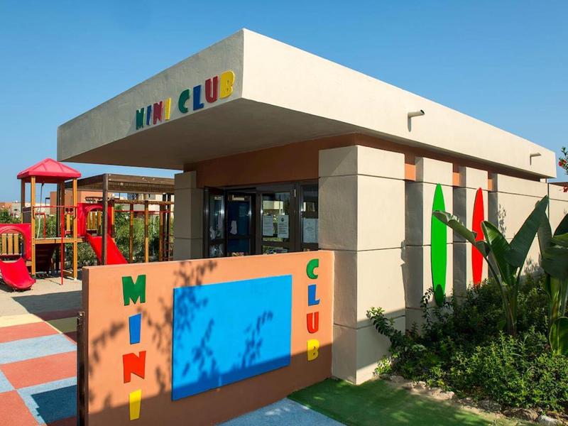 Modernes Kinderspielehaus mit buntem Spielplatz und Begrünung unter blauem Himmel.
