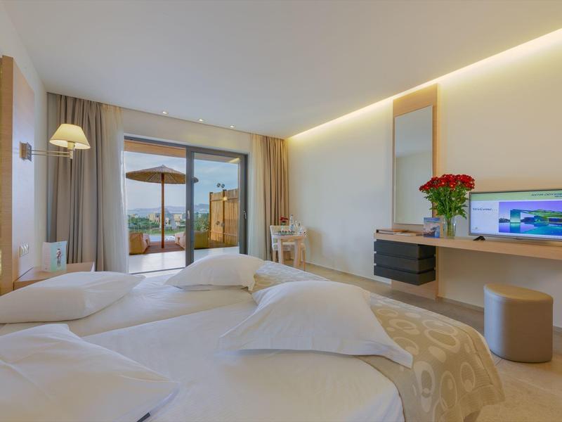 Hell eingerichtetes Hotelzimmer mit Doppelbett, TV, Schreibtisch und Balkon mit Blick ins Freie.