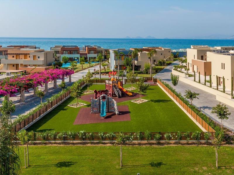 Blick auf eine Hotelanlage mit Gärten, Spielplatz und Meer im Hintergrund.