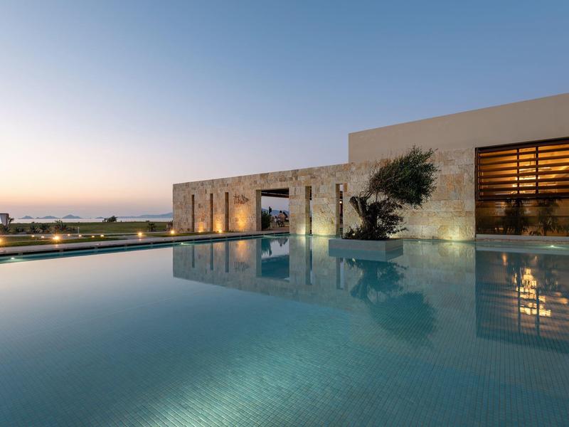 Moderner Pool mit ruhigem Wasser vor einem Gebäude bei Sonnenuntergang.