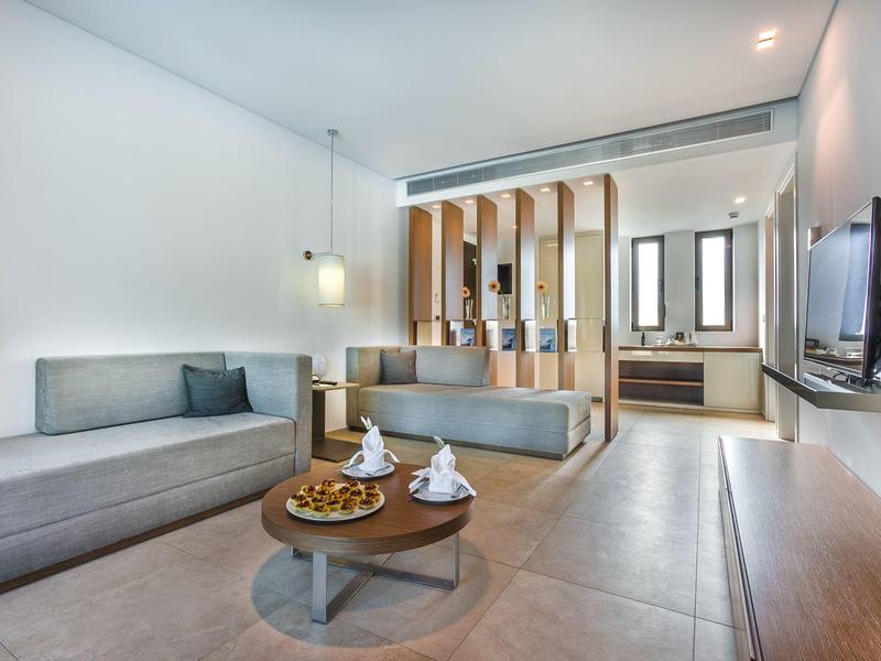 Modern eingerichtetes Wohnzimmer mit grauem Sofa, runden Holztisch und dekorativen Elementen.