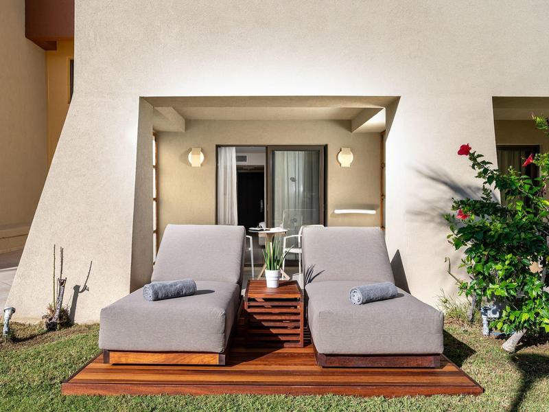 Zwei graue Liegestühle mit Holzboden vor einem Hotelzimmer mit Balkon und Garten