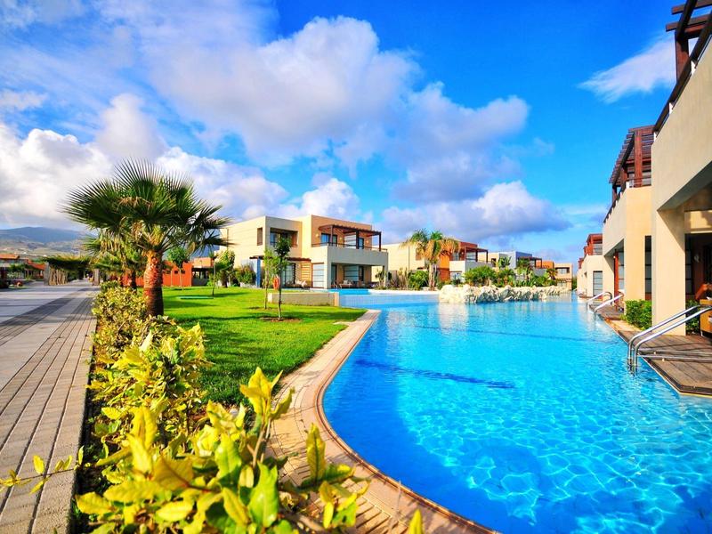 Moderner Hotelpool mit klarem blauem Wasser und gepflegtem Garten unter blauem Himmel.