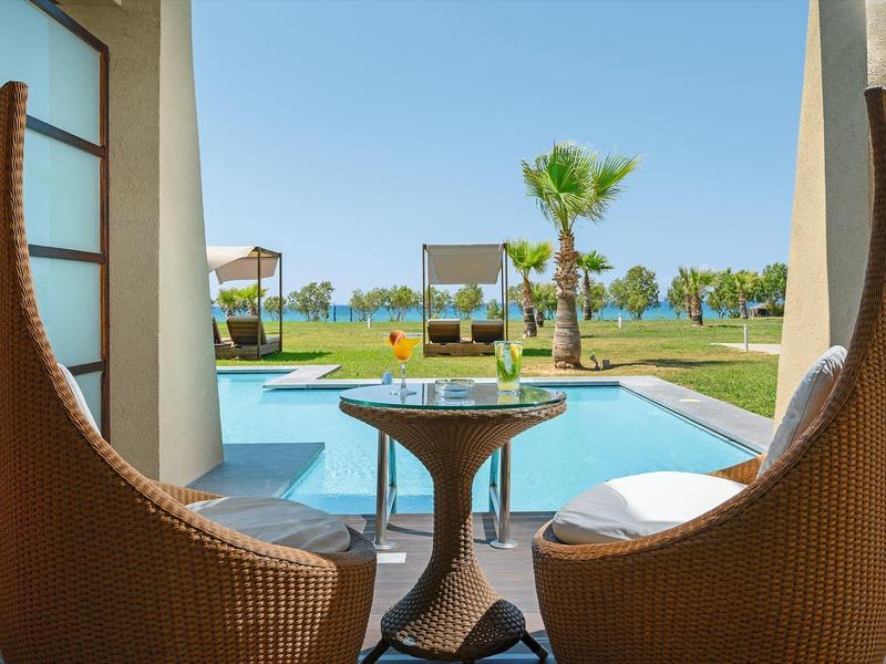 Zwei Geflechtstühle und ein Tisch auf einer Terrasse mit Pool und Gartenblick