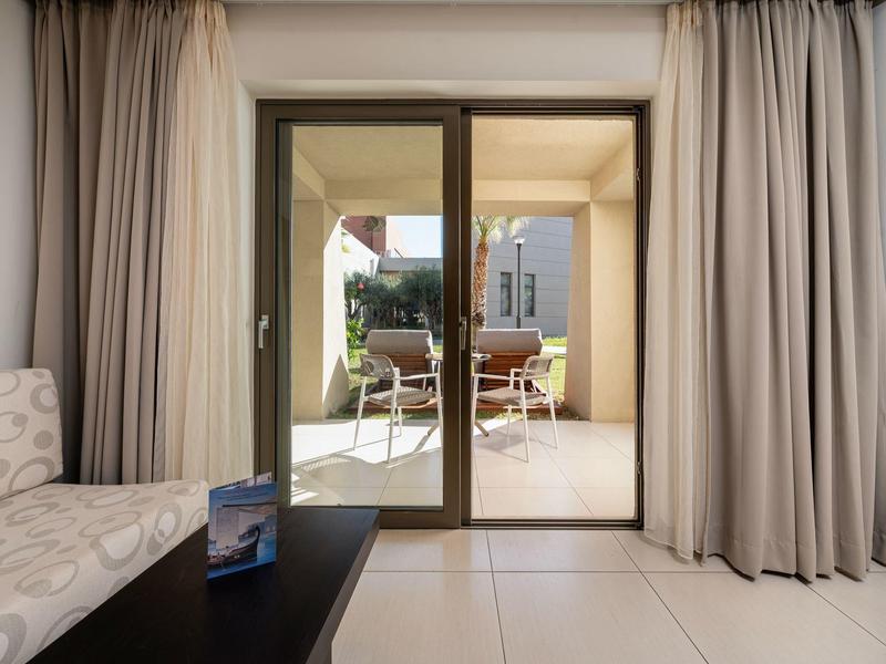 Blick von einem Wohnzimmer mit Sofa auf eine Terrasse mit Tisch und Stühlen hinter Glasschiebetüren.