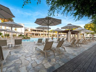 Espace piscine extérieur avec chaises longues et parasols devant un bâtiment hôtelier en plein jour.