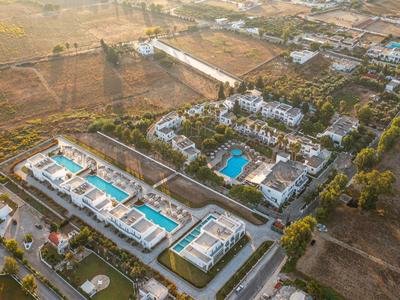 Vue aérienne d'un complexe hôtelier avec plusieurs piscines et des champs environnants au coucher du soleil.