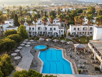 Piscine bleue entourée de chaises longues devant un hôtel blanc avec palmiers.