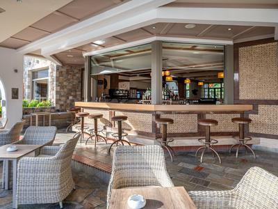 Accogliente area esterna con sgabelli da bar e mobili in rattan sotto una copertura.