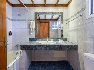 Salle de bain lumineuse avec lavabo, grand miroir, baignoire et toilettes.
