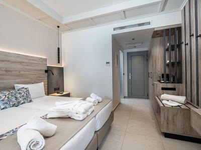 Chambre d'hôtel moderne avec deux lits, décoration claire et couloir étroit avec armoires.