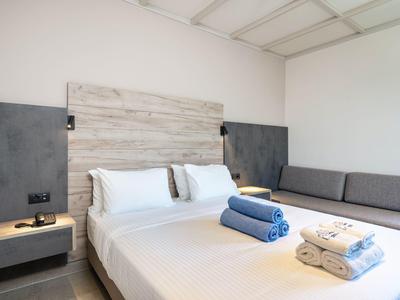 Nowoczesny pokój hotelowy z białym łóżkiem, szarą sofą i ręcznikami na łóżku.