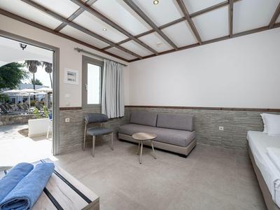 Jasny pokój hotelowy z tarasem, szarą sofą, łóżkiem i małym stolikiem.