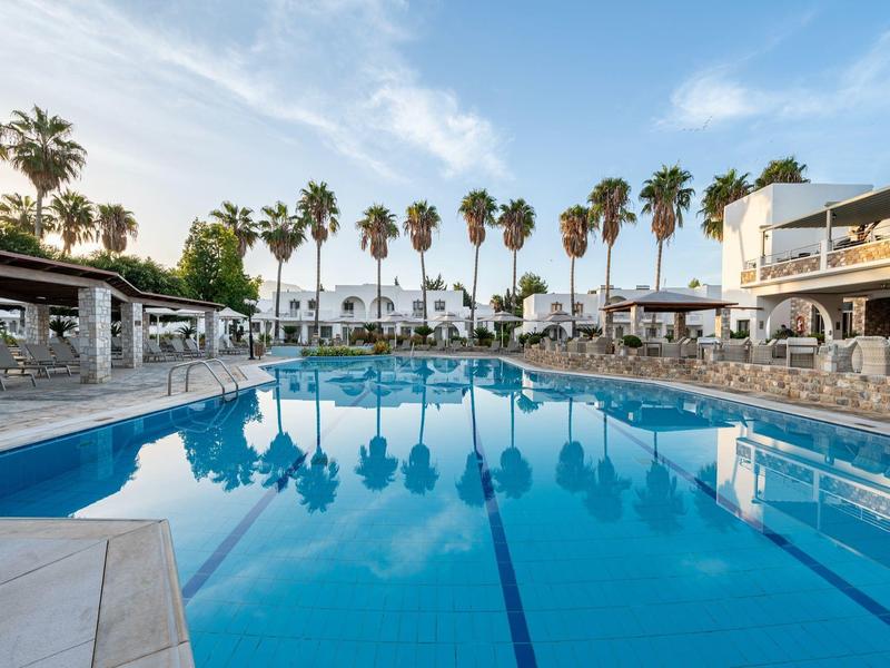 Grande piscine d'hôtel avec palmiers et chaises longues sous un ciel bleu.