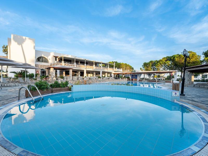 Piscine ronde d'hôtel sous un ciel bleu avec des transats et des bâtiments en arrière-plan.
