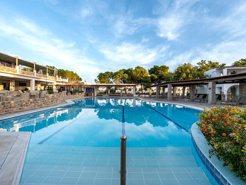 Grande piscine extérieure avec eau claire et terrasse ensoleillée sous un ciel bleu et des arbres.