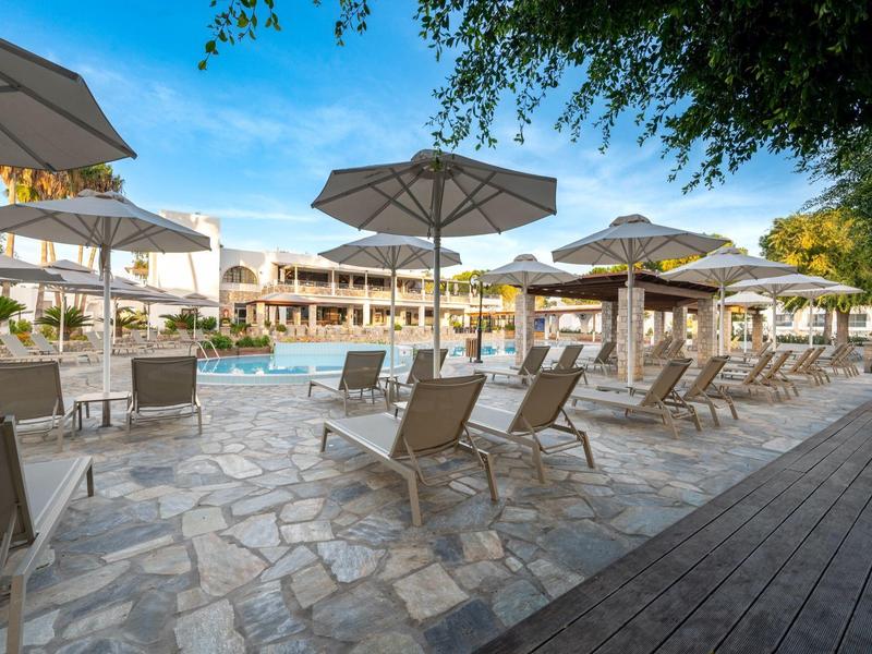 Espace piscine extérieur avec chaises longues et parasols devant un bâtiment hôtelier en plein jour.