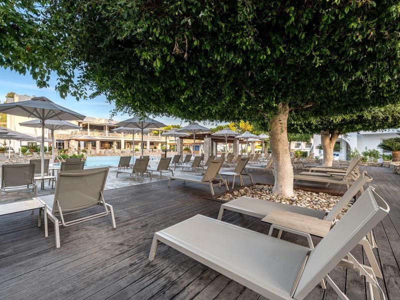 Terrasse ensoleillée avec chaises longues et ombre sous de grands arbres dans une station.