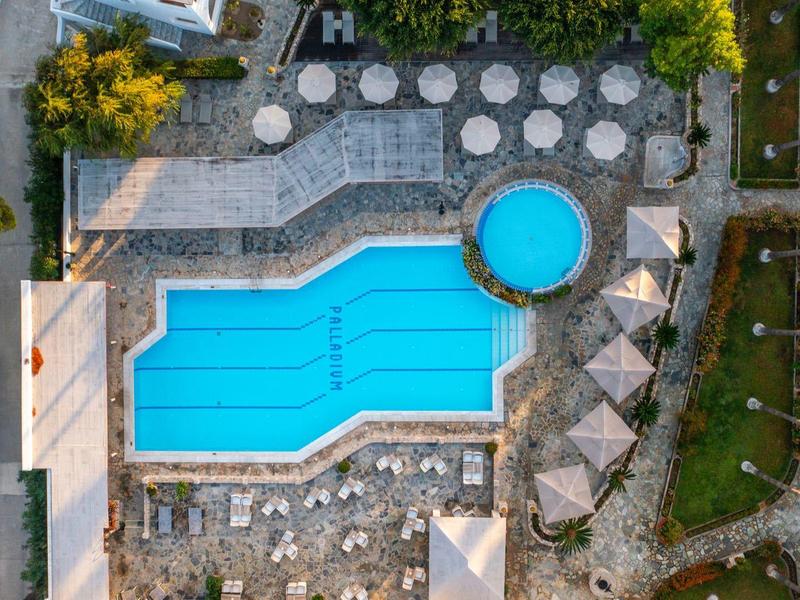 Vue aérienne d'une piscine d'hôtel avec chaises longues et parasols, entourée d'arbres.