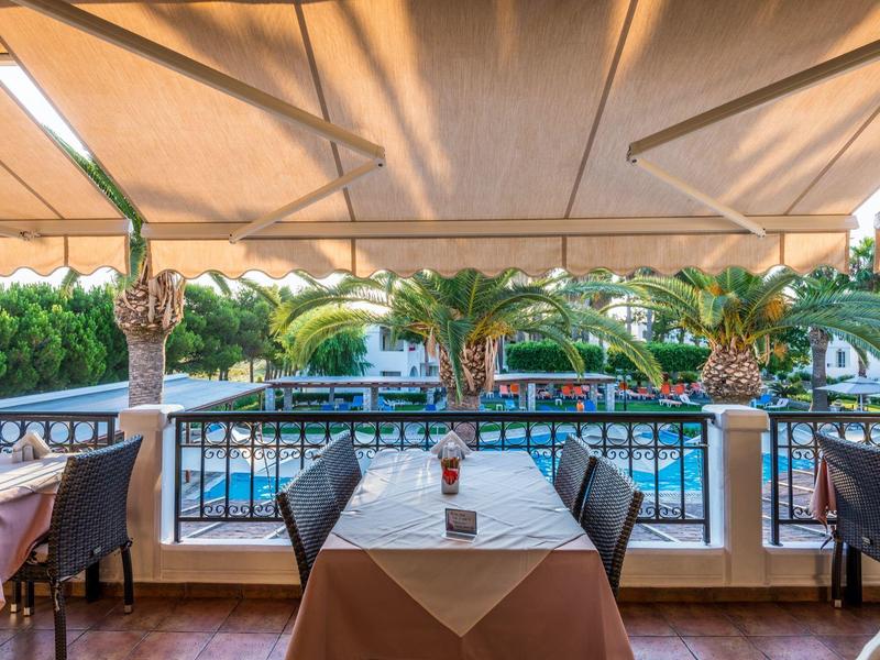 Terrasse avec table dressée, vue sur piscine et palmiers, ambiance chaleureuse d'hôtel.