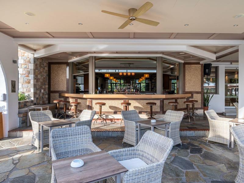 Bar moderne avec fauteuils en osier et tables en bois dans un espace ouvert et aéré.