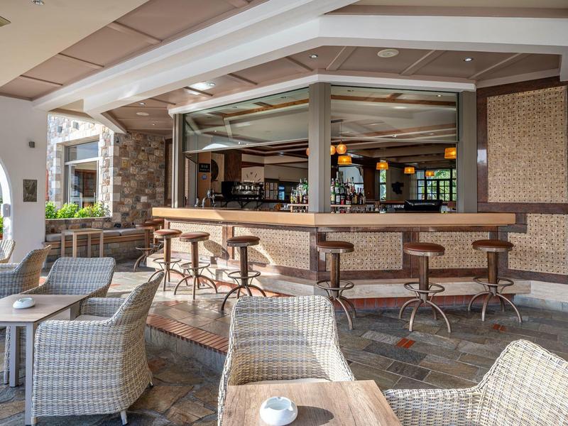 Bar d'hôtel confortable avec comptoir, barman et sièges en rotin.