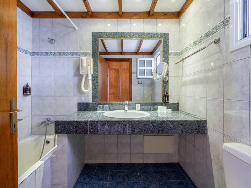 Salle de bain lumineuse avec lavabo, grand miroir, baignoire et toilettes.
