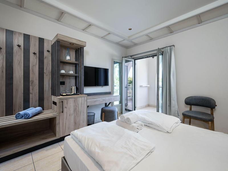 Chambre d'hôtel moderne et lumineuse avec lit double, meubles en bois et balcon extérieur.