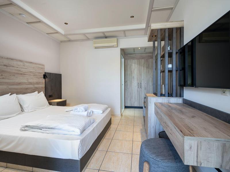 Chambre d'hôtel lumineuse avec lit double, télévision à écran plat et mobilier moderne en bois.