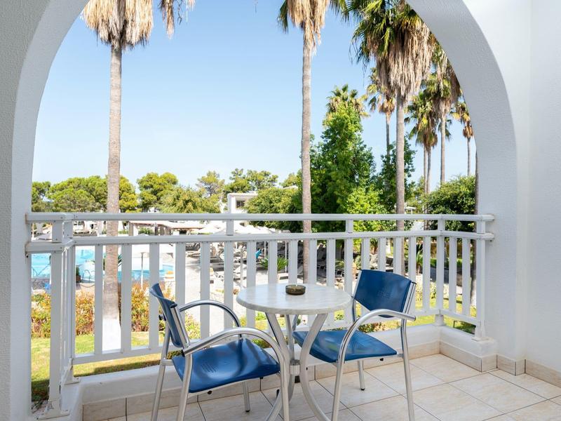 Balcon avec ensemble de chaises bleues et vue sur des palmiers et la piscine.