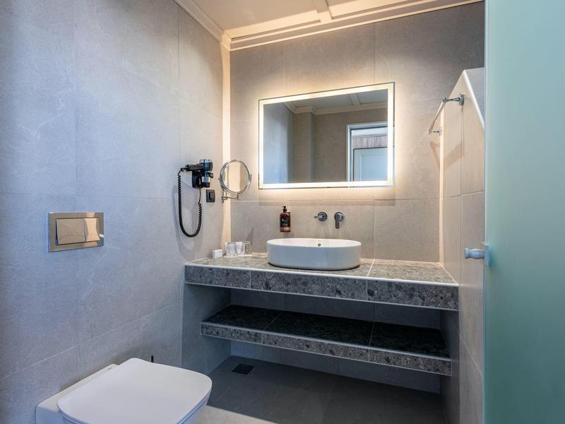 Salle de bains moderne avec miroir éclairé, lavabo et sèche-cheveux mural.