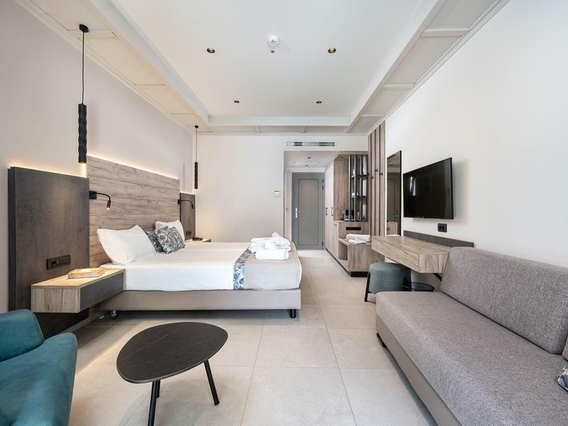 Chambre d'hôtel moderne avec grand lit, canapé gris et décoration minimaliste.