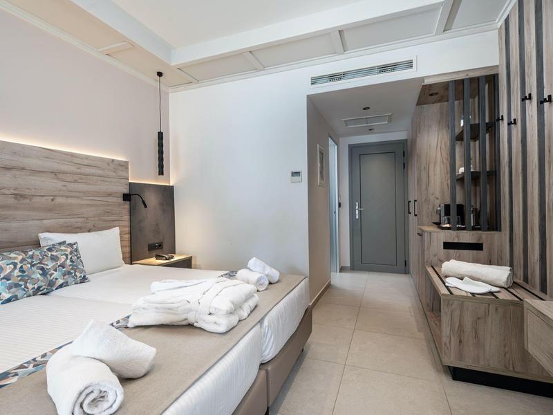 Chambre d'hôtel moderne avec deux lits, décoration claire et couloir étroit avec armoires.