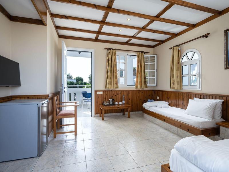 Chambre d'hôtel lumineuse avec sol carrelé, meubles en bois et balcon donnant sur la verdure.