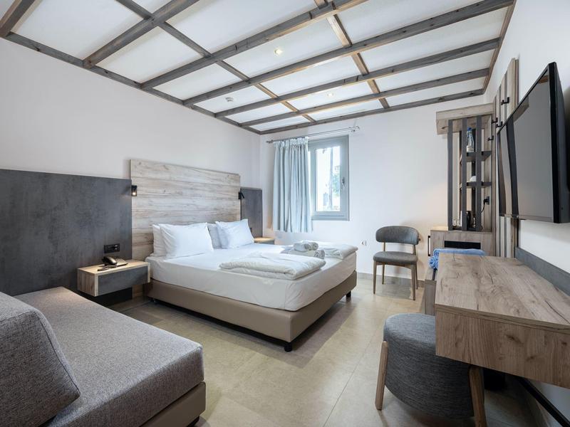 Nowoczesny pokój hotelowy z łóżkiem podwójnym, sofą, biurkiem i telewizorem na ścianie.