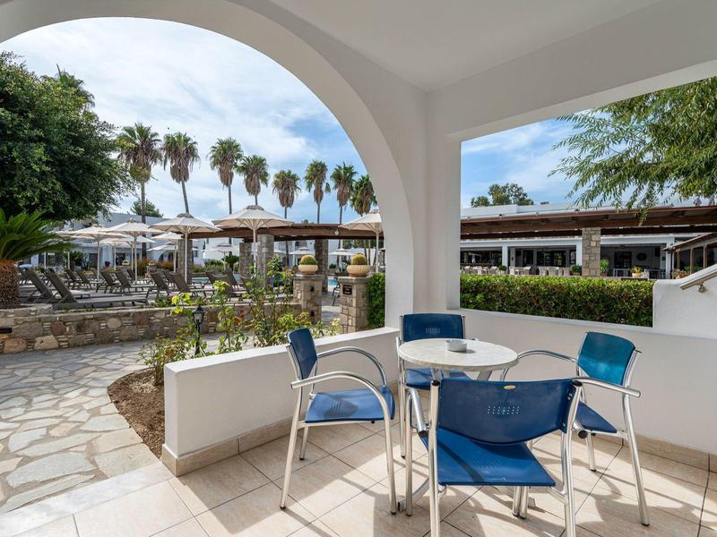 Espace assis avec mobilier bleu sous une arche blanche avec vue sur des palmiers et des bâtiments.