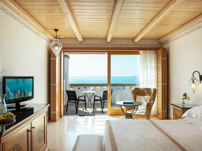 Camera d'hotel luminosa con vista mare e balcone con posti a sedere.