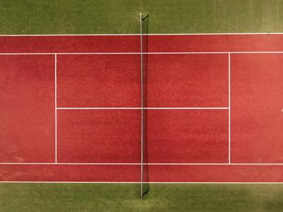 Vogelperspektive eines roten Tennisplatzes mit zwei Spielern und umgeben von grünem Gras.