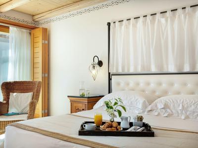 Camera d'hotel accogliente con letto grande, vassoio per la colazione e poltrona vicino al balcone.