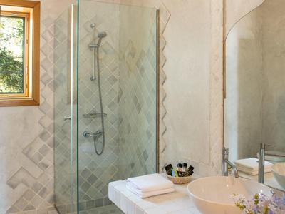 Bagno moderno con doccia in vetro, lavabo in pietra bianca, specchio e asciugamani turchesi.