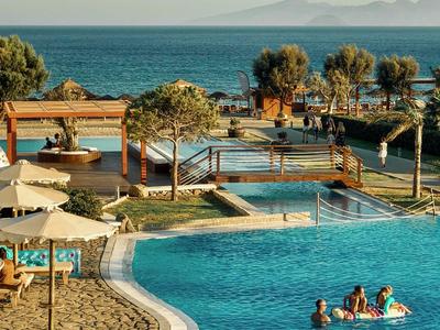 Hotelpool mit Gästen und Meerblick, Palmen und Sonnenschirmen im Hintergrund.