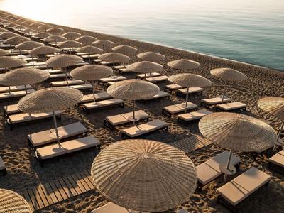 File di ombrelloni e lettini su una spiaggia sabbiosa vicino a acqua calma al tramonto.