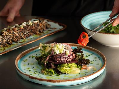 Elegantes Gericht mit gegrilltem Tintenfisch und grünen Salaten auf blauem Teller serviert